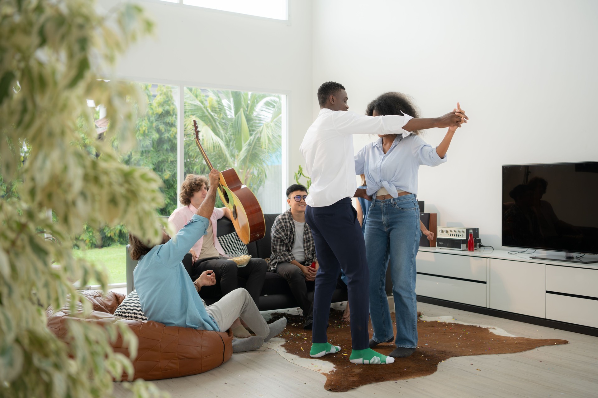 Group of multiethnic friends having fun at party by playing guitar, singing and dance together at home.